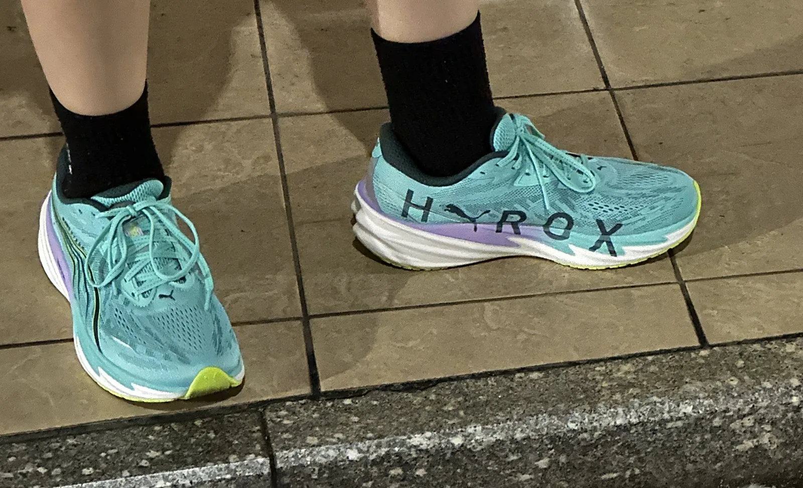 PUMA x HYROX ヴェロシティ ニトロ 5 を履いて屋外の歩道に立っている足元の写真。黒い靴下にミントグリーンの靴で、内側のHYROXの文字が見える